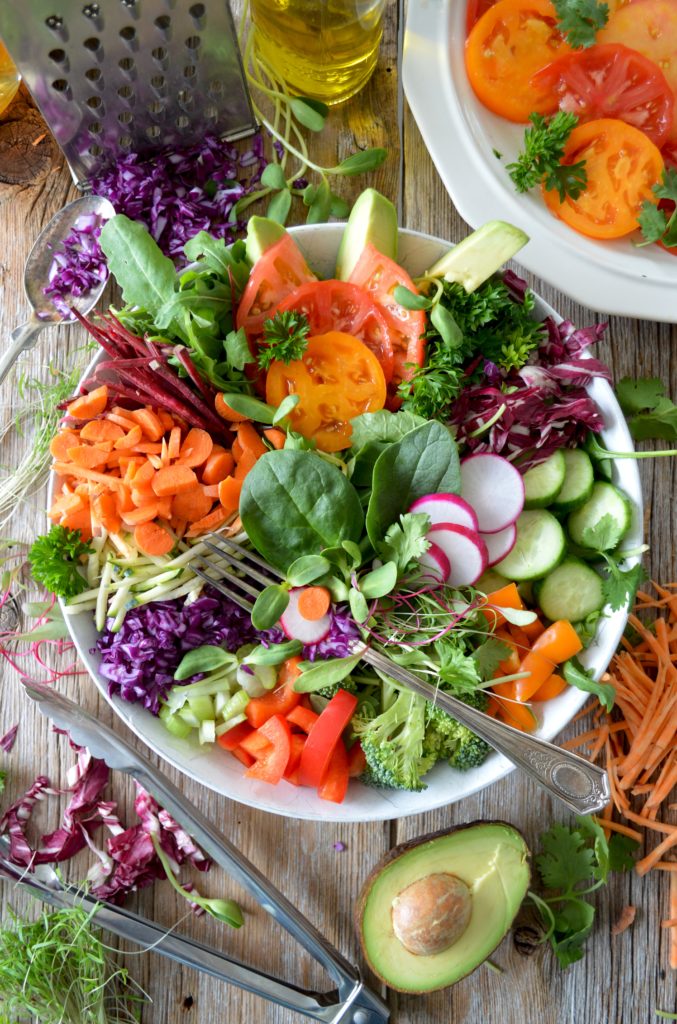 colorful bowl of salad greens tomatoes carrots radish and radicchio fork and avocado