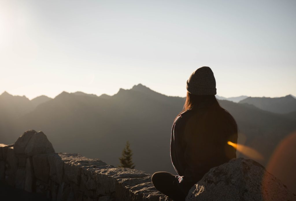 woman sitting on a mountain looking away at the sunrise